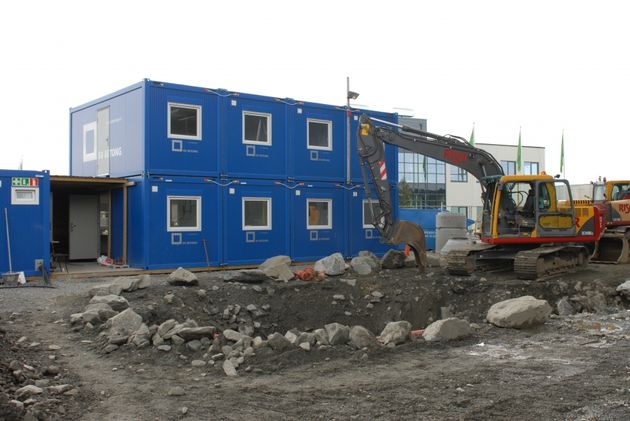 Blå brakker i 2 etasjer med gul gravemaskin utenfor